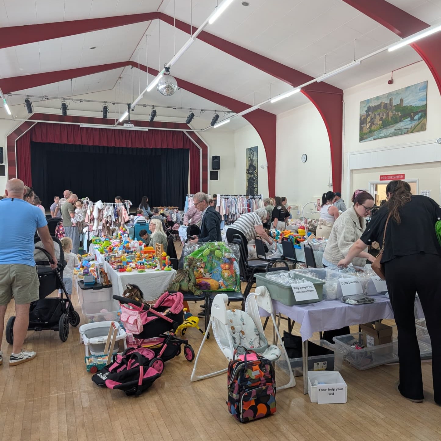 Families browsing stalls of children's clothes, books and toys at a busy market hall